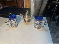 Full view of two tankards and covered vase on table