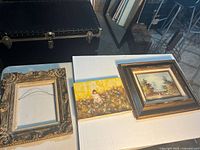 Group shot of two paintings and empty frame on table