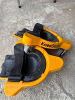 Two Milescraft KneeBlades stacked, side view shows orange body, black strap and one caster