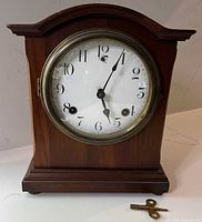 Front view of dark wood mantel clock with key on surface