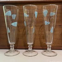 Front view of three footed pilsner glasses showing turquoise and gold amoeba-boomerang designs