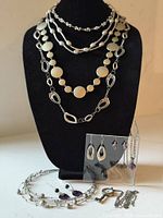 Layered silver-tone necklaces and acrylic stand holding amethyst set and abstract earrings
