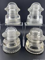Front view of four clear glass insulators showing brand markings