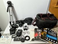 Overall view of lot showing cameras, tripod, flash, filters, books, bag, manuals