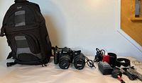 Overall view of backpack, camera body with lens, spare lens, charger, cords and accessories