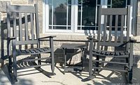 Two dark gray wooden rocking chairs and matching side table outdoors against stone wall