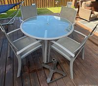 Round glass patio table with four chairs and umbrella stand base on deck
