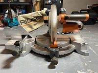 Left side view of RIDGID miter saw showing dust bag, blade guard, base and adjustment knobs