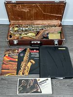 Closed case open displaying saxophone body, neck, accessories and music books