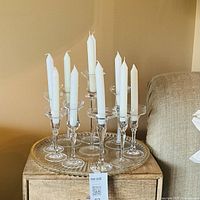 Ten clear glass candle holders with white taper candles on clear round tray