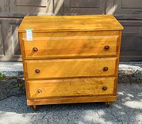 Front view of wooden dresser showing three drawers, knobs, finish wear