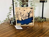 Front view of layered wooden Kingston map showing frame, layered contours, blue water, size reference tag