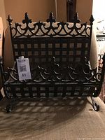Front view of black wrought iron log holder showing lattice body, decorative crest and scroll legs