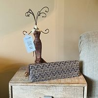 Jewelry holder mannequin with wire arms and patterned clutch sitting on wooden table