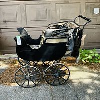 Full side view of black curved body pram with cane panel and four spoke wheels