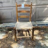 Full view of wooden ladder-back chair showing three back slats, woven rush seat, legs and stretchers