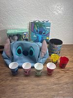 Group shot of all items: backpack, vinyl figure box, notebook, mug, four shot glasses