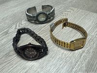 Three watches laid out: silver cuff, dark Armitron, gold Seiko