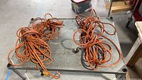 Two coiled orange extension cords on metal table