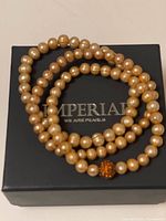 Three golden pearl bracelets, one with pavé bead, arranged on Imperial branded box