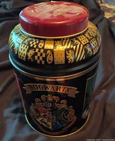 Full view of cylindrical Hogwarts tea tin with red lid and gold motifs