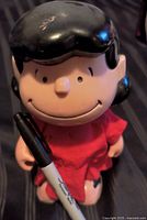 Front view of vintage Lucy Peanuts doll holding marker for scale