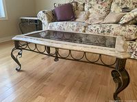 Oblique view of table showing glass insert, stone frame and wrought-iron legs