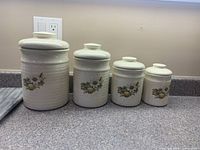 Four graduated ceramic canisters with floral fruit motif displayed on countertop