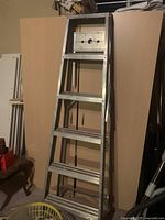 Aluminum step ladder with six rungs leaning against boards