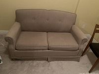 Front view of beige two-seat sofa bed with cushions and skirted base