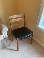 First teak dining chair with black seat in corner