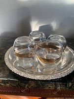 Four roly-poly glasses with gold bands on an ornate silver-plate tray