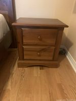 Angle view of wooden two-drawer nightstand showing top, drawers, and base