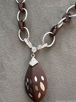 Close-up of pendant showing wood teardrop with silver inlays and stone-set sterling bail