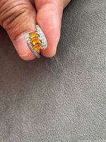 Ring held between fingers showing front view of three orange stones and accent stones