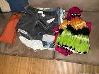 Stack of assorted denim shorts with orange shirt and tie-dye dress