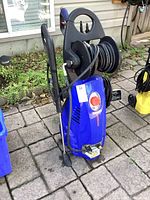 Front view of Simoniz S1900 pressure washer with hose reel, trigger gun and spare wand visible