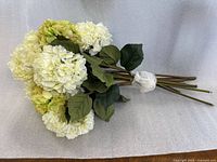 Side view of bundled ivory/cream hydrangea bouquet showing blossoms, stems, leaves, and plastic tie
