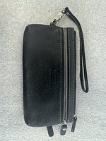 Front view of black pebbled leather wristlet wallet showing two zip compartments, detachable strap, embossed logo