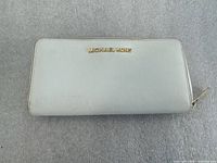 Front view of light beige Michael Kors wallet showing logo and gold-tone zipper