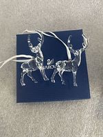 Two crystal reindeer ornaments lying on closed blue Swarovski box