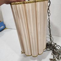 Vertical view of lamp shade showing ribbed cream body, gold trim, attached chain and cord