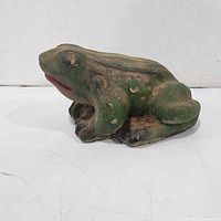 Left side view of painted concrete frog showing overall form and paint wear