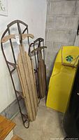 Two wooden runner sleds and yellow plastic sled leaning against wall