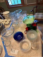 Overview of assorted glassware on table: casserole, mixing bowl, baking dish with green lid, colored mugs, stemware, bowls