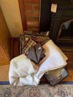 Stacked linens beside fireplace showing packaged plaid comforter set, folded ivory blanket, quilted white cover