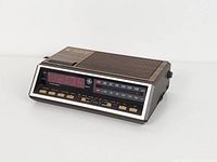 Three-quarter left view of GE digital clock radio showing woodgrain case, front display, buttons and AC cord