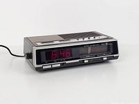 Left-front view showing red LED time, analog radio dial, woodgrain top, power cord