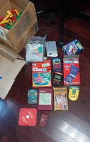 Overview of travel games laid out on floor showing board game boxes, handheld units and marble maze pieces