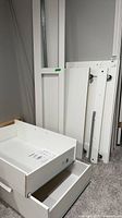 Disassembled white bed panels, drawer boxes and rails leaning against wall